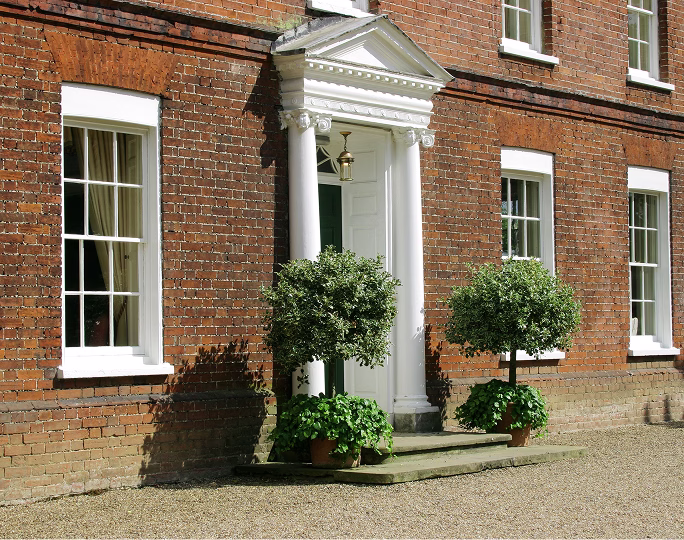 Entrance to a Georgian red-brick country house with a white columned portico, sash windows and bay trees, remortgaged on an interest-only basis