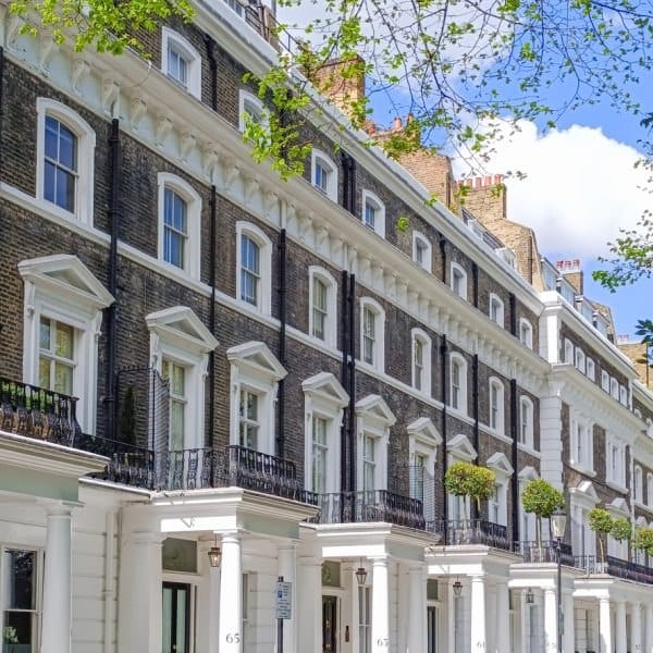 Row of period London terraced townhouses on a tree-lined street under a blue sky