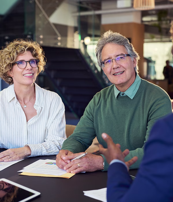 Smiling couple meeting a mortgage adviser to discuss complex income mortgage options, reviewing financial documents at a table