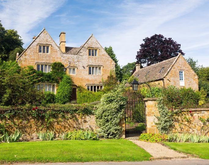 Cotswold stone period house with gabled roofs, climbing plants and a gated garden wall