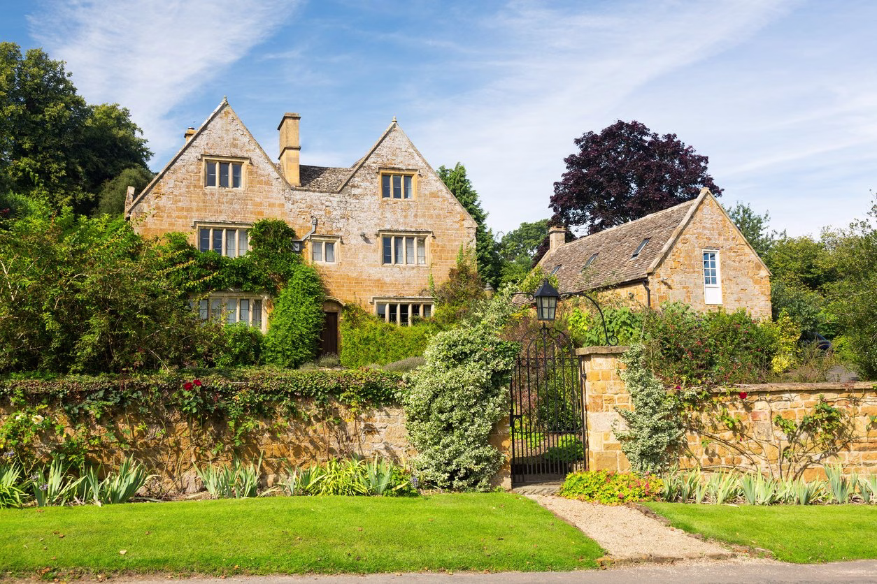 Cotswold stone period house with gabled roofs, climbing plants and a gated garden wall